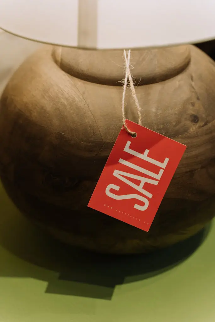Close-up of a rustic wooden lamp base with a red sale tag hanging, perfect for retail promotions.